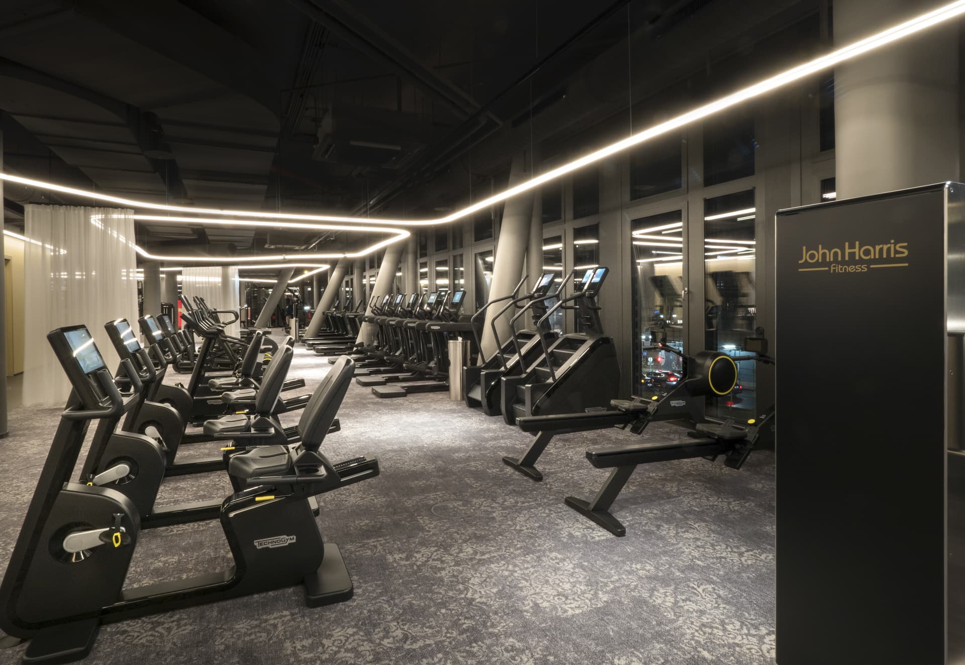 John Harris Fitness mit geschwungener Lichtlinie und textilem Raumteiler an einer gebogenen Schienenführung
